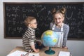 Geography lesson: A boy and a girl are sitting on a desk and studying the globe on the background of a school board. Royalty Free Stock Photo