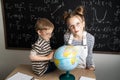 Geography lesson: A boy and a girl are sitting on a desk and studying the globe on the background of a school board. Royalty Free Stock Photo