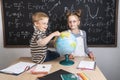 Geography lesson: A boy and a girl are sitting on a table and studying the globe on the background of a school board. Royalty Free Stock Photo