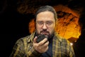 A geologist man in clean clothes with glasses holds in his hand a piece of coal on a blurred cave background.