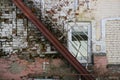 Geometric pattern of a straight iron staircase on the background of a brick wall with several layers of paint and a window