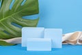 Geometric platform podiums and monstera leaf on blue background with pastel silk satin cloth