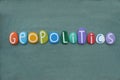 Geopolitics, creative text composed with multi colored stone letters over green sand Royalty Free Stock Photo