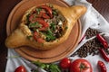 Georgian khachapuri with meat and tomatoes on a round kitchen board