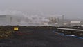 Geothermal power station Svartsengi with steaming chimneys and sign beside moss-covered lava field on cloudy day in winter.