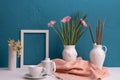 Gerbera, daffodils, white frame for a photo, a cup with coffee and a teapot and two vases with a cotton plant on a blue background Royalty Free Stock Photo