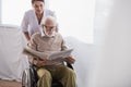 Nurse near elderly handicapped man reading