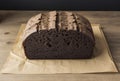 German black bread is on craft paper, wooden table. Dark bread with malt added. One of most popular types of bread in Germany
