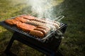 German Bratwurst sausages and marinated pork neck steak meat roasting with smoke on foldable charcoal BBQ barbecue grill in garden Royalty Free Stock Photo