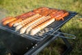 German Bratwurst sausages and marinated pork neck steak meat roasting with smoke on foldable charcoal BBQ barbecue grill in garden Royalty Free Stock Photo