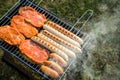 German Bratwurst sausages and marinated pork neck steak meat roasting with smoke on foldable charcoal BBQ barbecue grill in garden Royalty Free Stock Photo