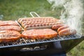 German Bratwurst sausages and marinated pork neck steak meat roasting with smoke on foldable charcoal BBQ barbecue grill in garden Royalty Free Stock Photo