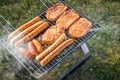 German Bratwurst sausages and marinated pork neck steak meat roasting with smoke on foldable charcoal BBQ barbecue grill in garden Royalty Free Stock Photo