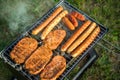 German Bratwurst sausages and marinated pork neck steak meat roasting with smoke on foldable charcoal BBQ barbecue grill in garden Royalty Free Stock Photo