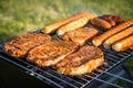 German Bratwurst sausages and marinated pork neck steak meat roasting with smoke on foldable charcoal BBQ barbecue grill in garden Royalty Free Stock Photo