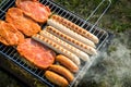 German Bratwurst sausages and marinated pork neck steak meat roasting with smoke on foldable charcoal BBQ barbecue grill in garden Royalty Free Stock Photo