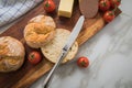 German fine veal liver sausage spread with two crispy bread rolls buns, tomatoes, butter and knife on wooden board, kitchen towel