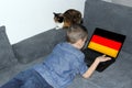 German flag on a laptop display, a little schoolboy in jeans lies on a sofa and scrolls, a cat sits nearby, a concept of learning