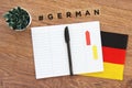 German flag, notebook, pen and inscription hashtag german on a wooden desktop, foreign language concept
