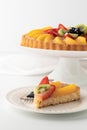 German fruit flan with one slice on a plate in front ready for eating.