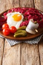 German Labskaus hearty dish of potatoes, corned beef and beetroot with fried egg, pickles and herring close-up on a plate.