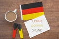 german national flag, notebook with the inscription learn german online, two markers, cup of coffee on brown wooden desktop