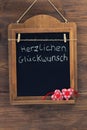 German text Herzlichen Glueckwunsch means Best Wishes written with chalk on aged blackboard with textile hearts hanging on wooden