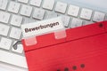 The German word for applications can be seen on the label of a red hanging folder. The hanging folder is on a computer keyboard Royalty Free Stock Photo