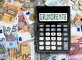 German word GRUNDRENTE basic pension written on display of pocket calculator against cash money on table