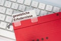 The German words for legal requirements can be seen on the label of a red hanging folder. The hanging folder is on a computer keyb Royalty Free Stock Photo