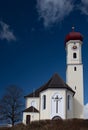 In Germany, in Bavaria, in a small village, there is a white chapel on a hill. The sky is blue. Next to the chapel is a bare tree Royalty Free Stock Photo