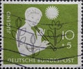 GERMANY - CIRCA 1956: This postage stamp in green shows a girl with a flute and with various symbols on a charity postal stamp for