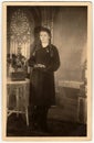 Vintage photo shows young woman poses with book, she stands next to the table with a bunch of flowers. Black white