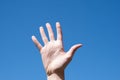 Gesture closeup of a woman`s hand showing five fingers, against a blue sky, sign language symbol number five