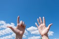 Gesture closeup of a woman`s hand showing one open palm and two fingers up on a blue sky background