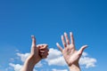 Gesture closeup of a woman`s hand showing one opened palm and thumb up  on a blue sky background with clouds Royalty Free Stock Photo