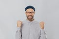 Gesture of success. Jubilant overjoyed unshaven man raises clenched fists, wears spectacles and formal shirt, celebrates his