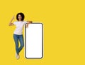 Gesturing OK young african american woman happy leaned on big, huge smartphone with white screen wearing white t-shirt Royalty Free Stock Photo