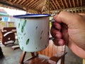 old fashioned enamel cup in white with green prints held in hand