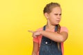 Get out! Portrait of angry upset little girl with braid in denim overalls pointing way out showing exit Royalty Free Stock Photo