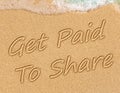 Get Paid To Share Sign on the sand on the beach with the sea washing up the shore