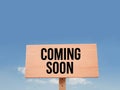 A wooden sign that says coming soon is against a blue sky.