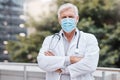 Get serious about wearing your mask. a mature male doctor standing with his arms crossed in the city. Royalty Free Stock Photo