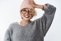 Getting all trendy this winter season. Portrait of charming blond european girlfriend in sweater and pink beanie pulling