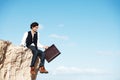 Getting away from it all. Smiling young businessman sitting with his legs dangling over the side of a cliff next to Royalty Free Stock Photo