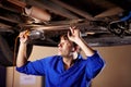 Getting a better look. A young male mechanic looking underneath a car with a light.