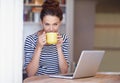 Getting a creativity boost from caffiene. a young woman working on her laptop and enjoying a cup of coffee at home. Royalty Free Stock Photo