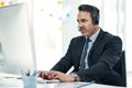 Getting his busy day sorted. a mature businessman using a headset while working on a computer in an office. Royalty Free Stock Photo