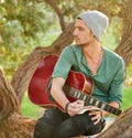 Getting musically inspired by nature. a handsome young man sitting in a park with a guitar writing song on a notepad. Royalty Free Stock Photo