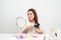 Getting rid of tangles. Beautiful young woman looking at her reflection in mirrorand brushing her long hair while sitting at the